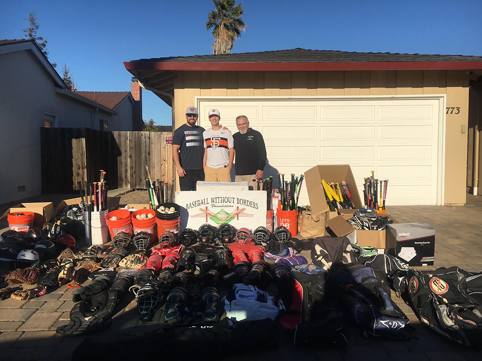Volunteers stand behind rows of donated baseball equipment for the Baseball Without Borders Foundation, a charity supported by Phases Financial Group.