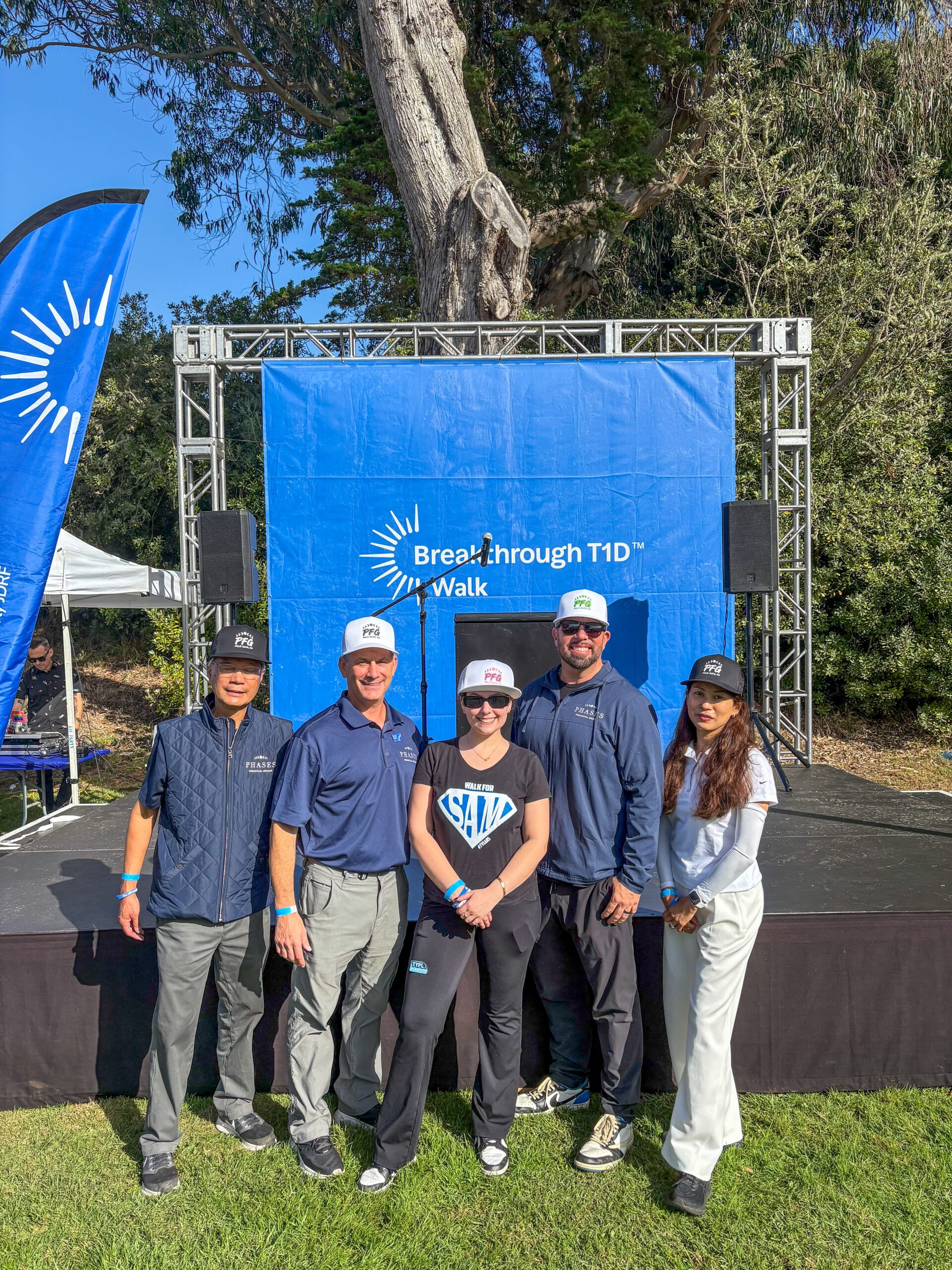 Phases Financial Group team members stand in front of the Breakthrough T1D Walk stage backdrop, wearing Phases-branded caps.