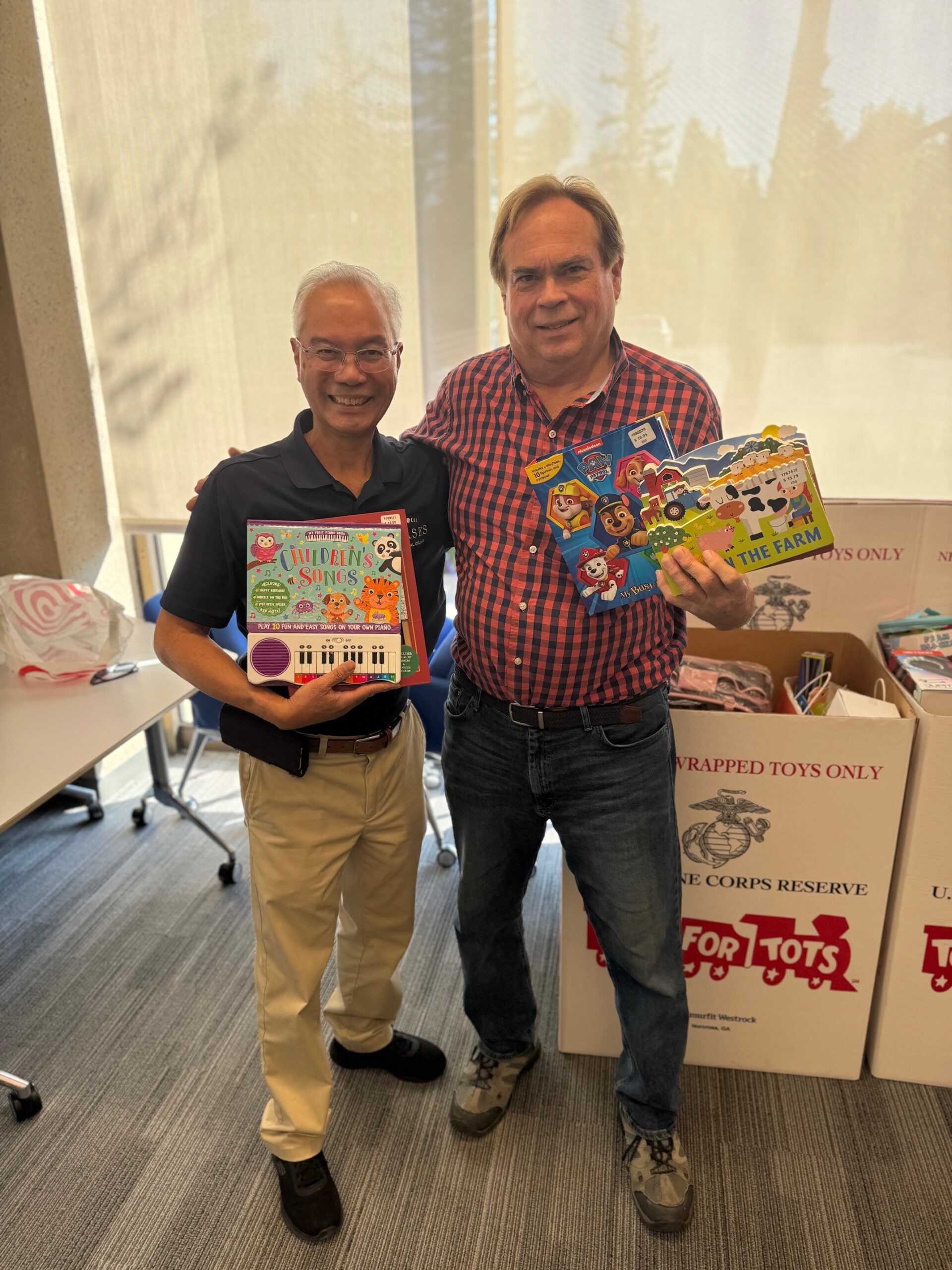 Frank Mueller and a friend hold donated children's books and toys for Phases Financial Group's Toys for Tots drive.