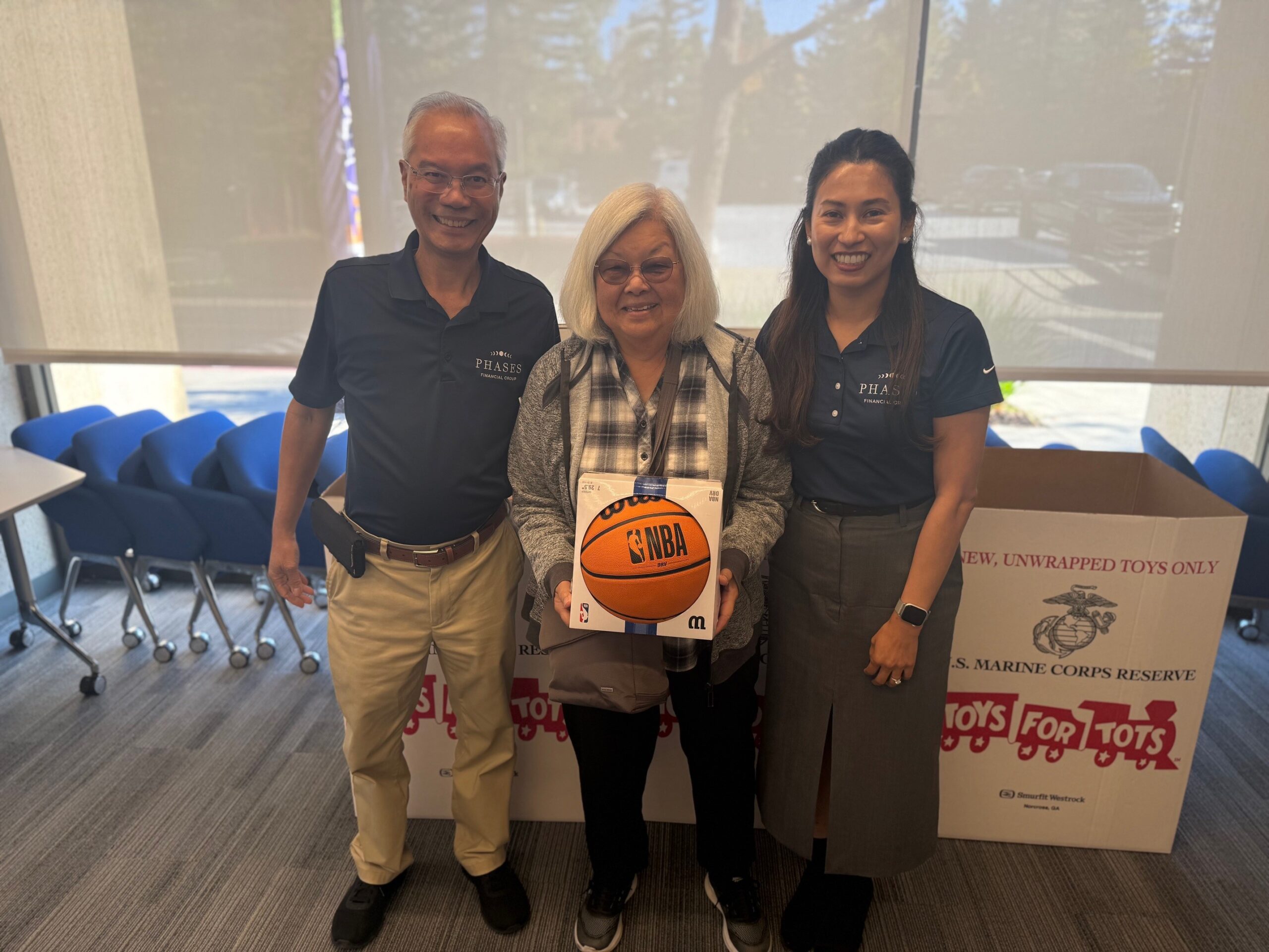Phyllis Nakano holds a donated basketball alongside two Phases Financial Group team members for the Toys for Tots drive.
